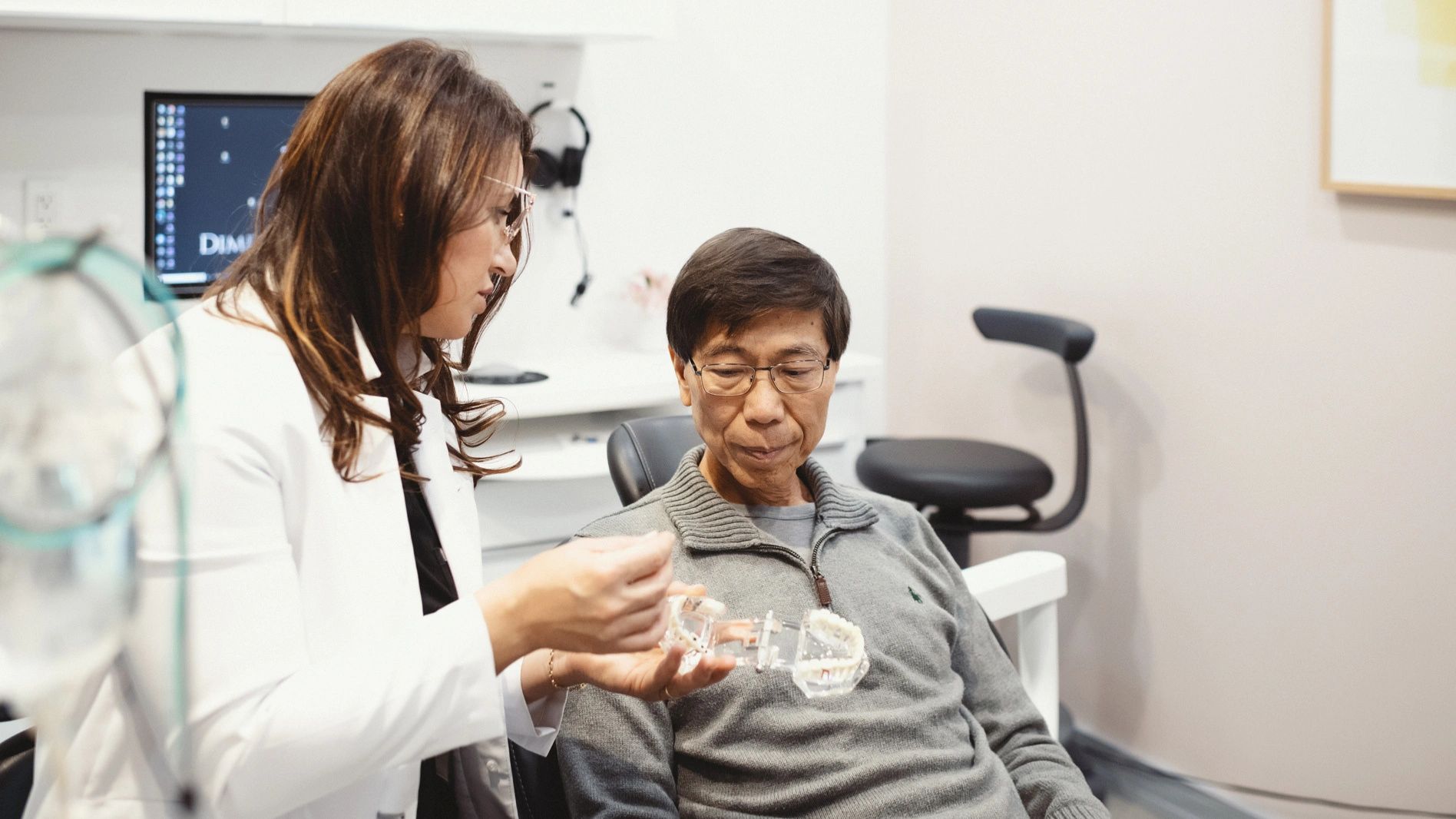 Dentist showing denture models to a patient in a Holmdel dental chair